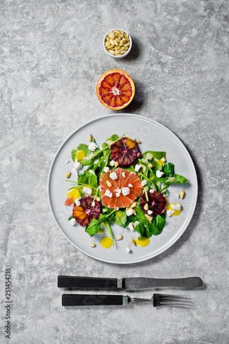Salad with arugula, grapefruit, red oranges, nuts and cheese on a plate. Grey background, top view