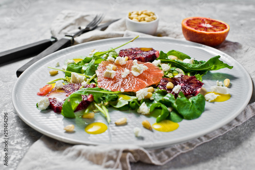 Healthy salad with arugula, grapefruit, red oranges, nuts and tofu cheese. Gray background, side view