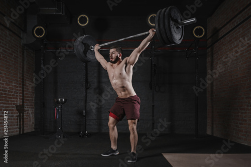 Crossfit athlete lifting barbell overhead at the gym. Shirtless man doing functional training. Practicing powerlifting.