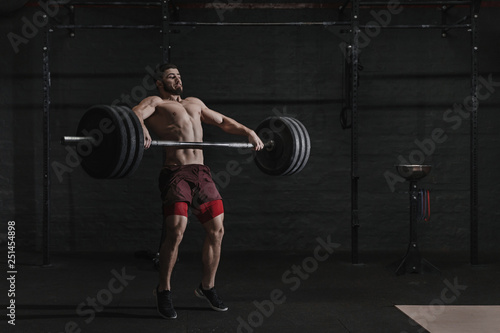 Muscular man lifting a barbell in crossfit gym.