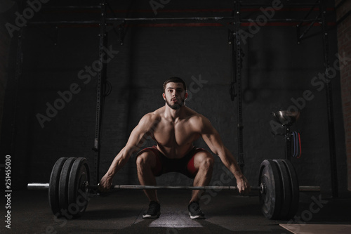 Young crossfit athlete lifting barbell at gym. Muscular shirtless man doing functional training. Deadlift exercise.