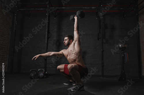 Crossfit athlete exercising at the gym doing overhead dumbbell squats.