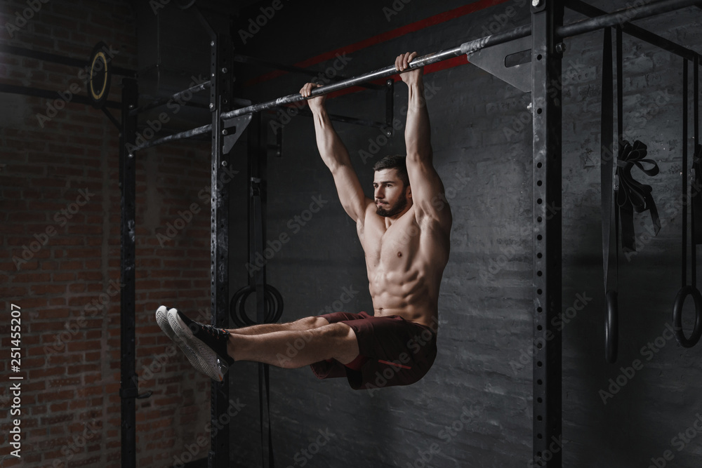 Crossfit athlete doing abs exercise on horizontal bar at the gym. Handsome man doing functional training workout. Practicing calisthenics. Stock Adobe Stock