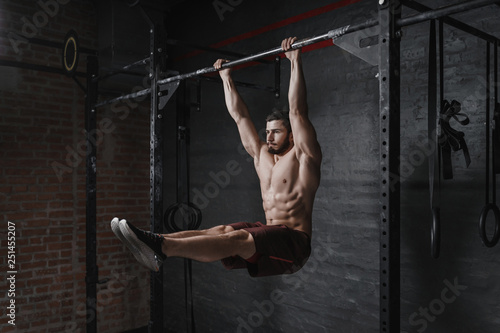 Crossfit athlete doing abs exercise on horizontal bar at the gym. Handsome man doing functional training workout. Practicing calisthenics. photo