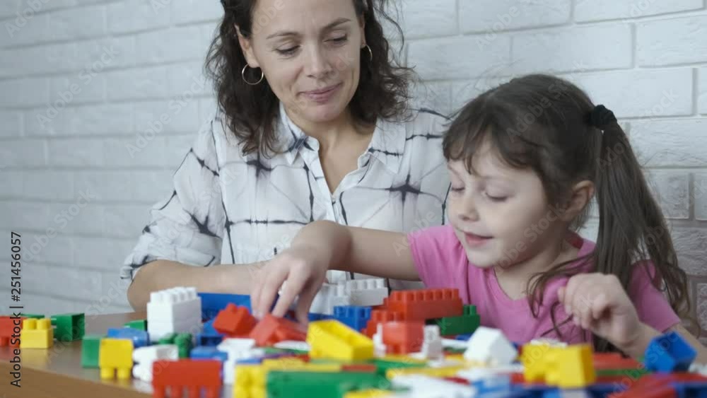 A child with mother plays in the designer. A cute little girl builds a house from the designer. A child with mother plays in the designer. A cute little girl builds a house from the designer.