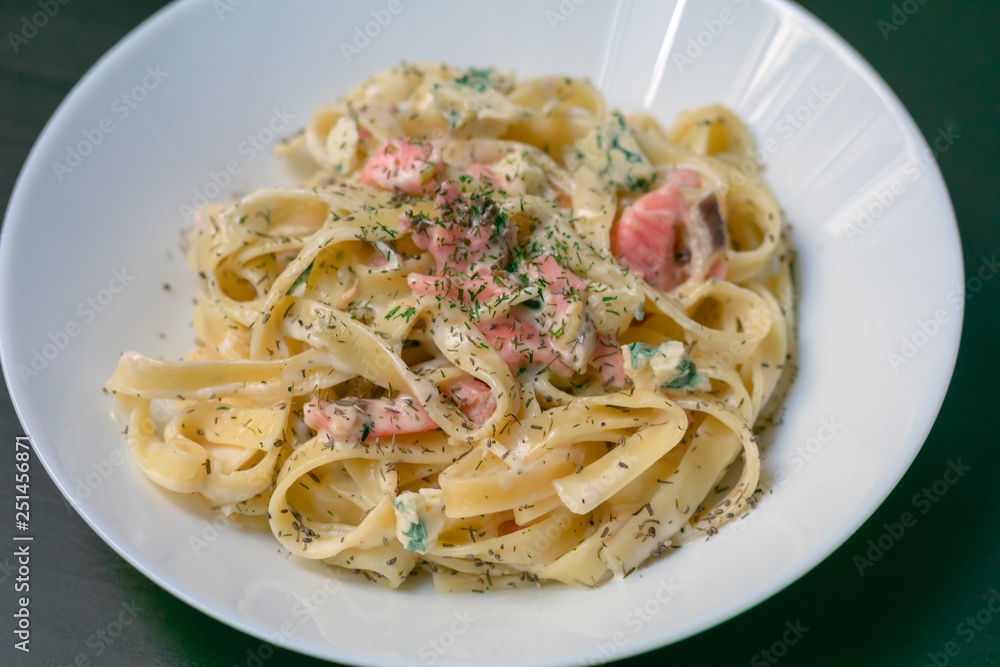 Homemade tagliatelle with salmon and dill on a black wooden table