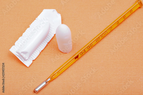 Thermometer and suppository medication on orange background. Rectal drug administration. photo