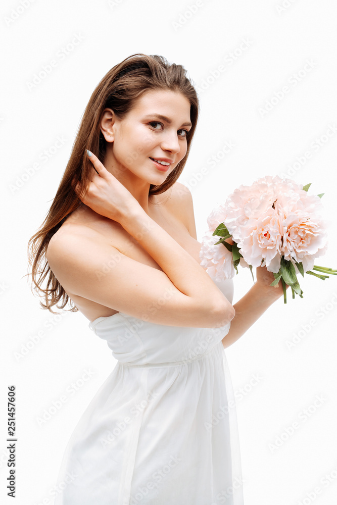Portrait beautiful young girl smiling and posing with artificial flowers on white background in white dress. Portrait beautiful young girl smiling and posing with artificial flowers on white background in white dress.