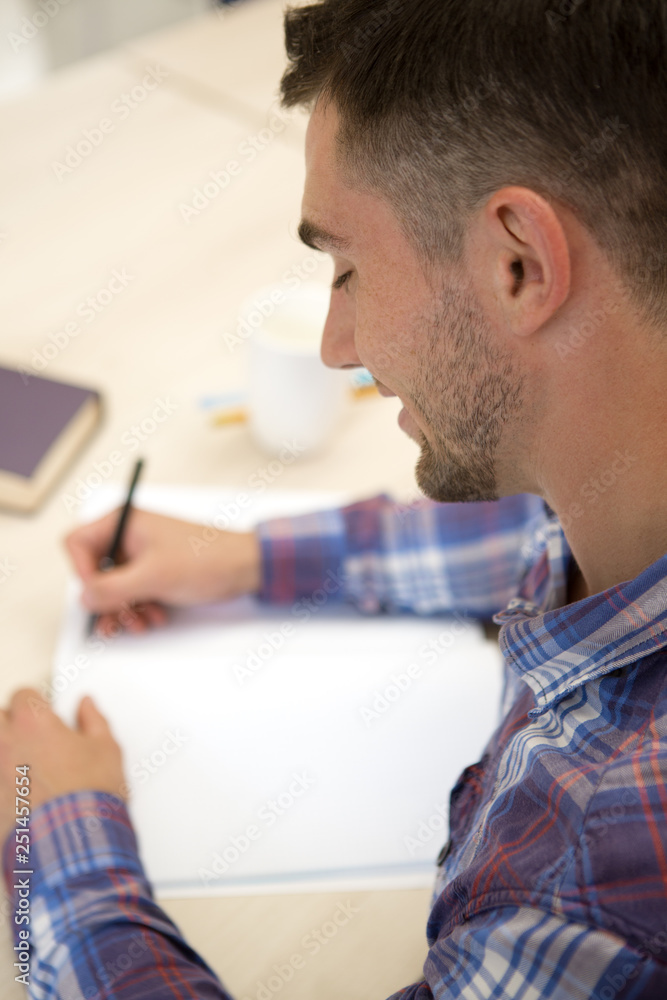 Crop of handsome boy sitting at table and writing homework in notebook. Crop of handsome boy sitting at table and writing homework in notebook.
