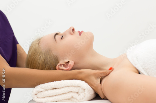Side view of relaxed female client lying on white couch during spa procedure in wellness center. Hands of qualified therapist massaging shoulders of woman. Concept of body care and treatment.