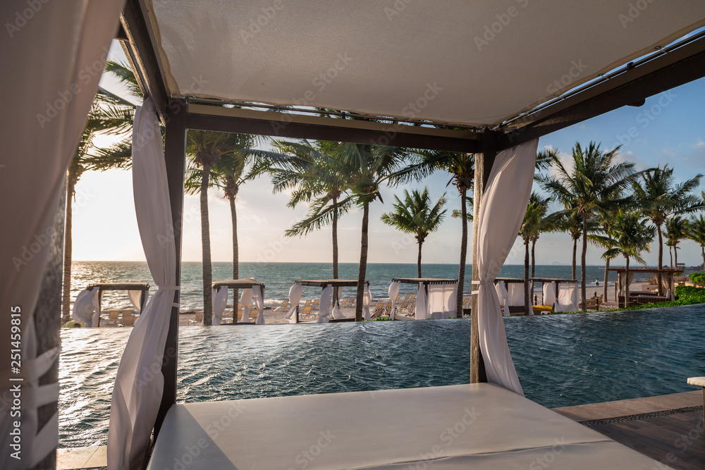 Private beds in a lounge area of a a high end Mexican resort overlooking the ocean at sunrise. - obrazy, fototapety, plakaty 