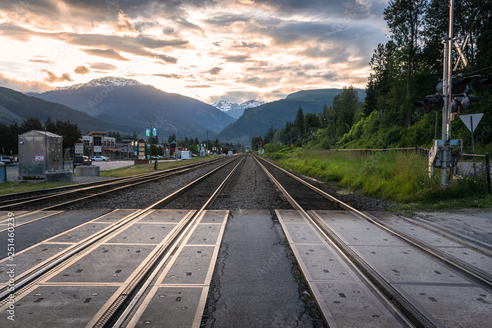 Parallel Railroad Tracks through a Town Centre with Towering Mountains in Background at Dusk. Revelstoke, BC, Canada.