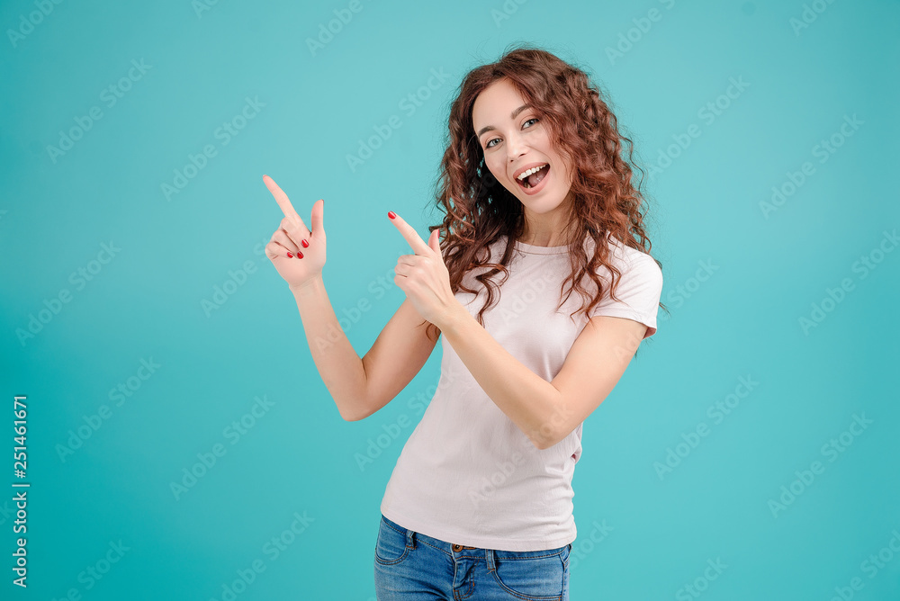 Fototapeta premium Attractive brunette girl with curly hair isolated over blue turquoise background pointing at a copy space above her head