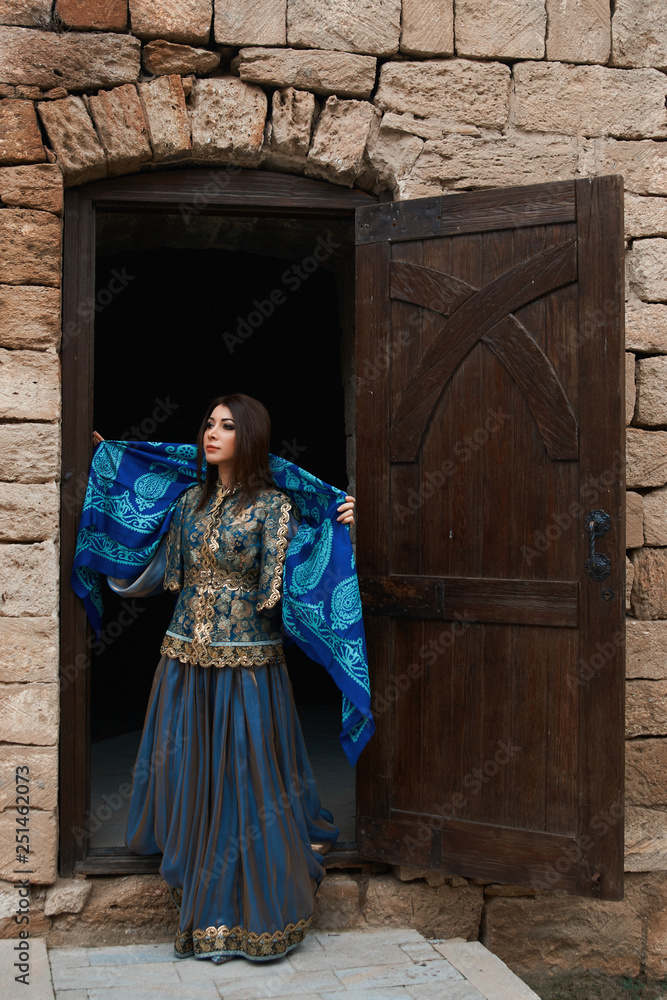 Beautiful girl in traditional dress comes out of the door of a brick house