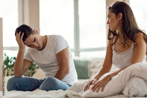 Young couple with relationship difficulties talking in bedroom.