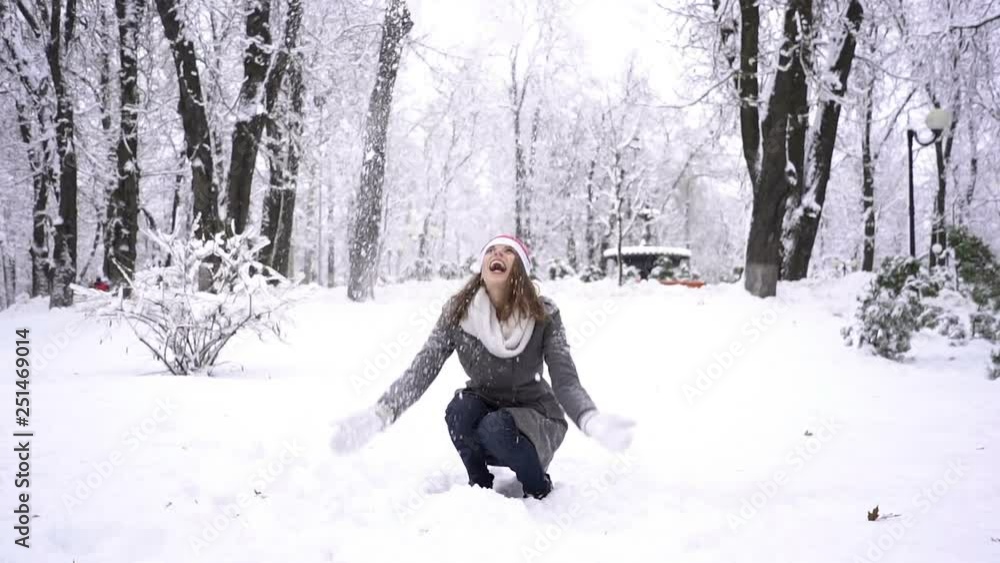 Young woman in Santa hat quickly throws snow up in city park. Slow motion Young woman in Santa hat quickly throws snow up in city park. Slow motion