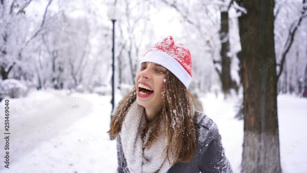Young woman in Santa hat and snow smile and play in winter city park. Slow motion portrait Young woman in Santa hat and snow smile and play in winter city park. Slow motion portrait
