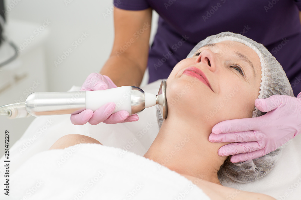 Closeup of woman face receiving anti aging hardware procedure in cosmetology office. Hands in gloves of dermatologist stroking facial skin with apparatus. Concept of cosmetology and beauty.