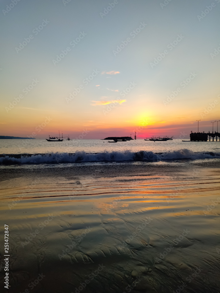 Fototapeta premium A very beautiful sunset reflected on the wet sand on the shores of the Indian Ocean, the pier and fishing ships can be seen. 26 february, Bali, Indonesia.