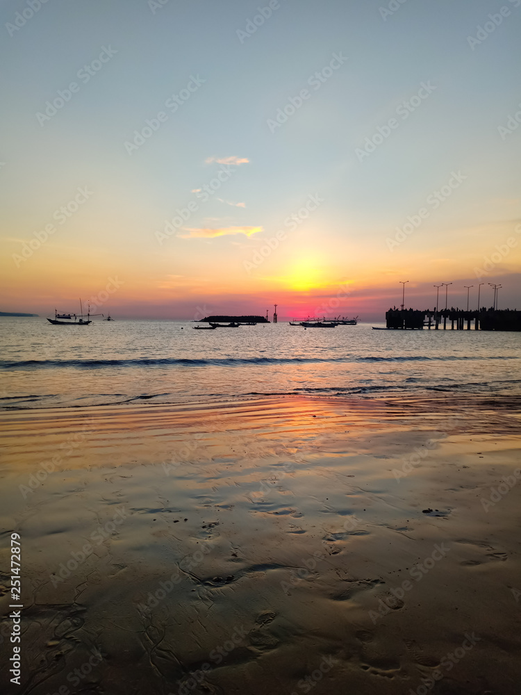 Fototapeta premium A very beautiful sunset reflected on the wet sand on the shores of the Indian Ocean, the pier and fishing ships can be seen. 26 february, Bali, Indonesia.