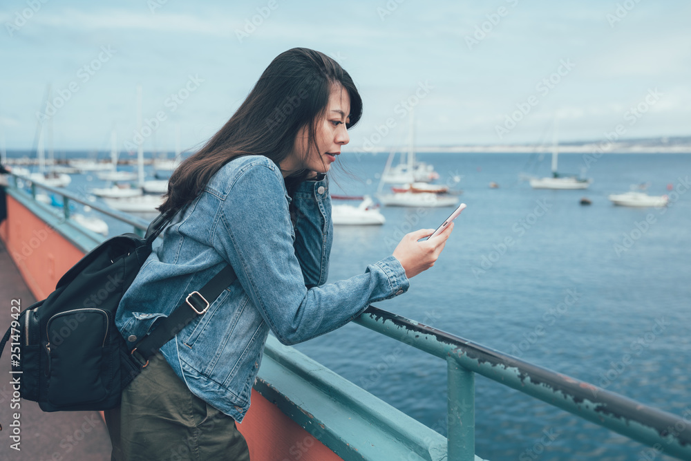 young local asian lady holding cellphone waiting for date in afternoon at beach bay. girl with backpack communicate friends chat on mobile phone seeing ocean boat view Old Fisherman's Wharf. young local asian lady holding cellphone waiting for date in afternoon at beach bay. girl with backpack communicate friends chat on mobile phone seeing ocean boat view Old Fisherman's Wharf.