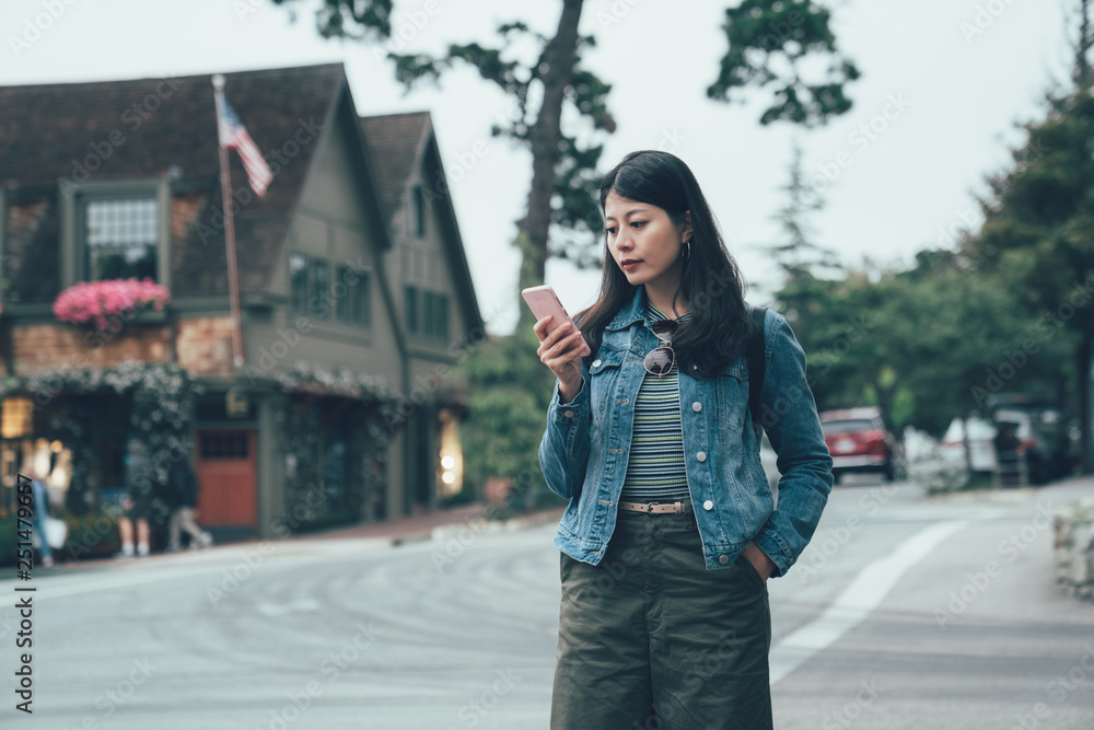 attractive asian woman traveler with mobile phone looking finding hotel direction on the city street in carmel by the sea california. young girl tourist on road with traditional american style house