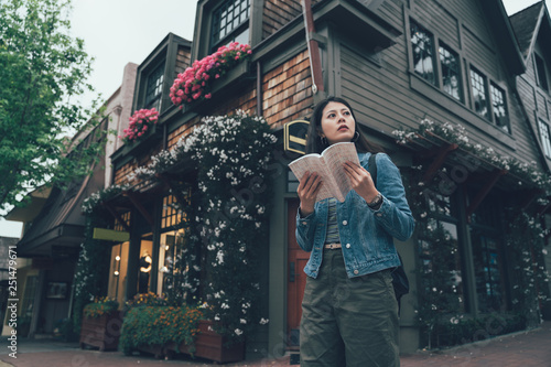 Φωτογραφία young asian female backpacker holding guide book standing by american style house with flower on corner in carmel by the sea california