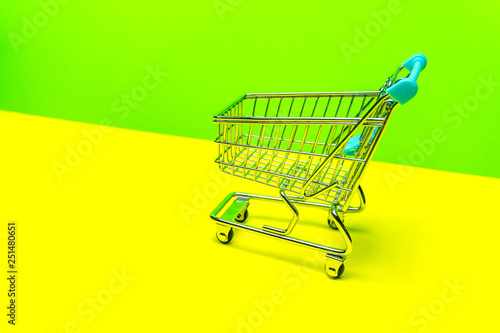 Miniature shopping cart on yellow green backdrop, retail shopping concept