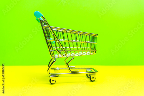 Miniature shopping cart on yellow green backdrop, retail shopping concept