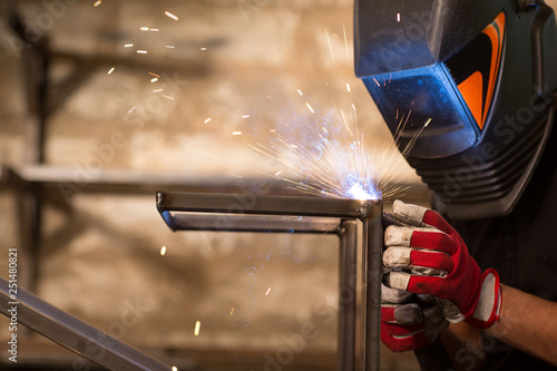 Man, wearing in welding mask, brewing metal with welding machine.