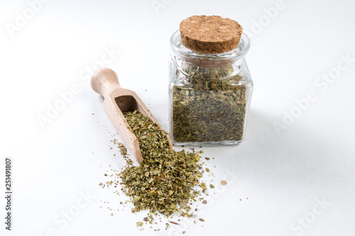 marjoram in wooden scoop and jar on isolated on white background