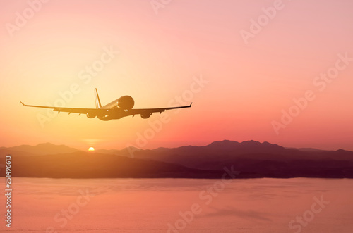 Airplane flying over tropical beach with sunset sky abstract background. © tonktiti