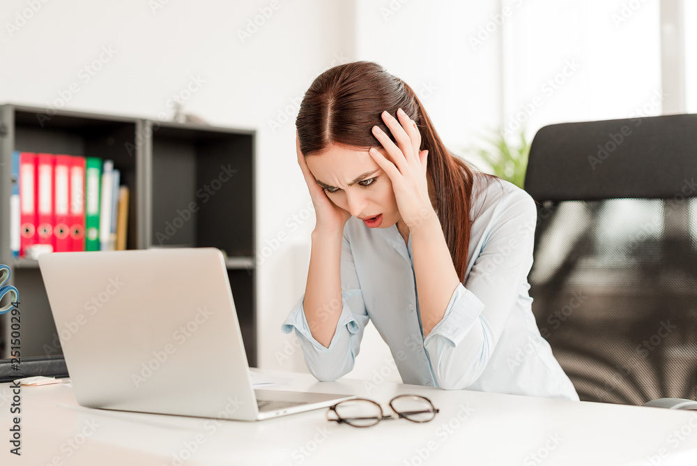 Business concept - confused young business woman sitting at her desk with the laptop in the office. Problems at work Business concept - confused young business woman sitting at her desk with the laptop in the office. Problems at work