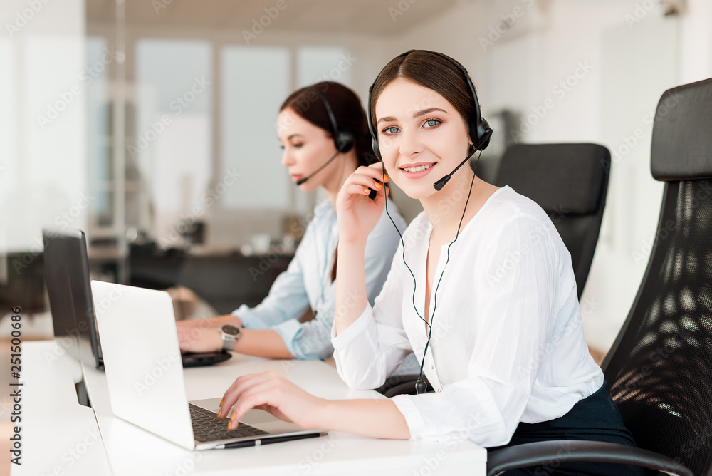 Friendly young female technical support dispatcher with a headset working in a call center on a hotline, talking on the phone. Portrait of an attractive customer care representative. Business concept Friendly young female technical support dispatcher with a headset working in a call center on a hotline, talking on the phone. Portrait of an attractive customer care representative. Business concept