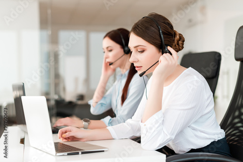 Friendly young female technical support dispatcher with a headset working in a call center on a hotline, talking on the phone. Portrait of an attractive customer care representative. Business concept