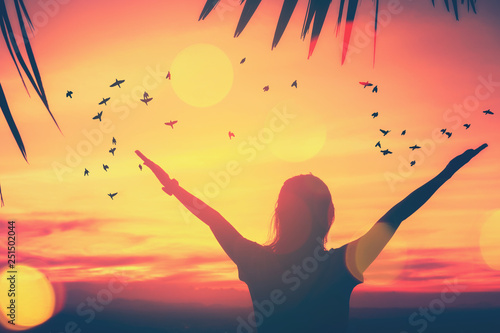 Freedom feel good and travel adventure concept. Copy space of silhouette woman rising hands on sunset sky double exposure colorful bokeh and bird fly background.