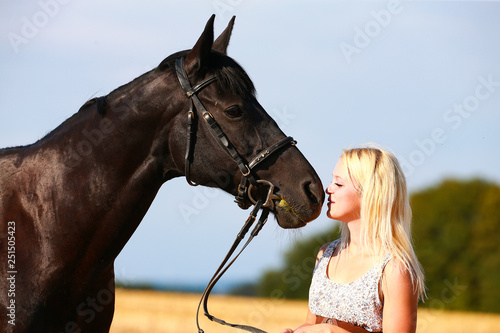 Horse with owner in portrait on a summer field, owner cuddles with her horse.