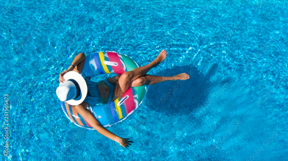 Beautiful girl in hat in swimming pool aerial top view from above, woman relaxes and swims on inflatable ring donut and has fun in water on family vacation, tropical holiday resort