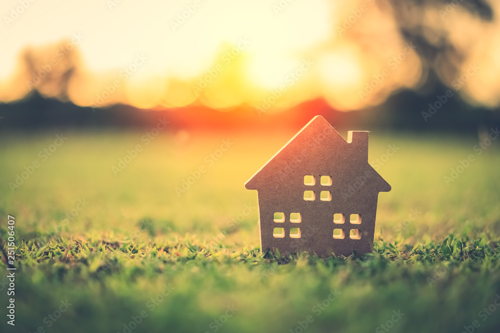 Obraz premium Skopiuj przestrzeń koncepcji domu i życia. Mały model domu na zielonej trawie z abstrakcyjnym tle światła słonecznego.