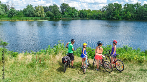 Family on bikes cycling outdoors, active parents and kids on bicycles, aerial view of happy family with children relaxing near beautiful river from above, sport and fitness concept