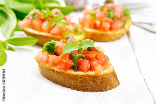 Bruschetta with tomato and spinach on light wooden board