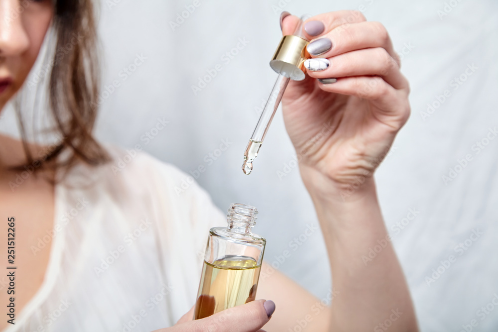 Fototapeta premium Pipette with drop of cosmetic oil and bottle in female hand, closeup