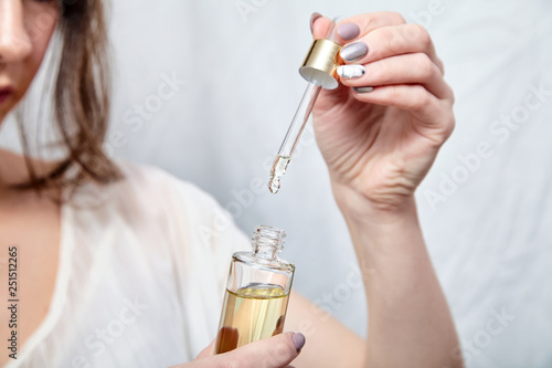 Pipette with drop of cosmetic oil and bottle in female hand, closeup