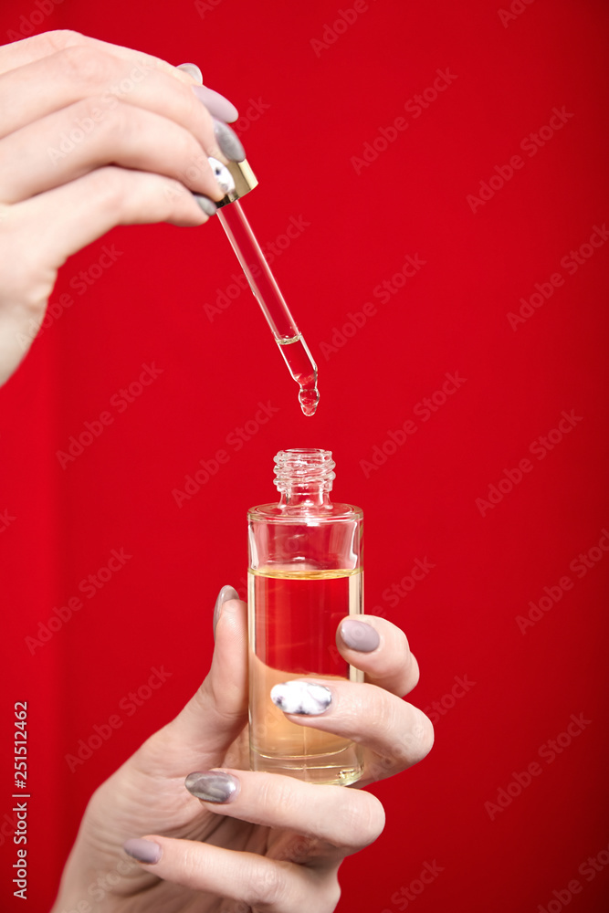 Φωτογραφία Pipette with drop of cosmetic oil and bottle in female hand on red background