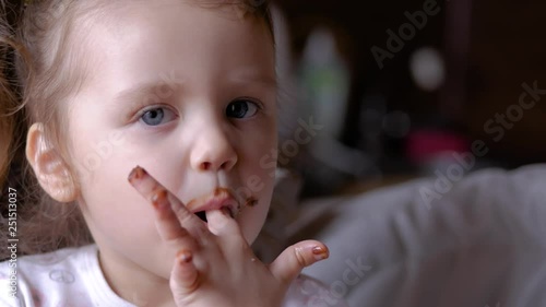 Child licking chocolate off her fingers. Funny small girl eating chocolate.