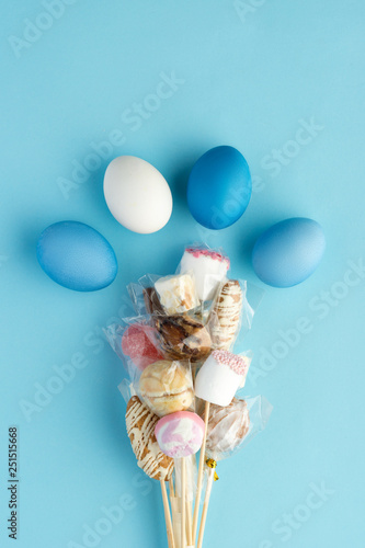 Painted eggs with bouquet of candies on blue background, top-view © Dmitrii