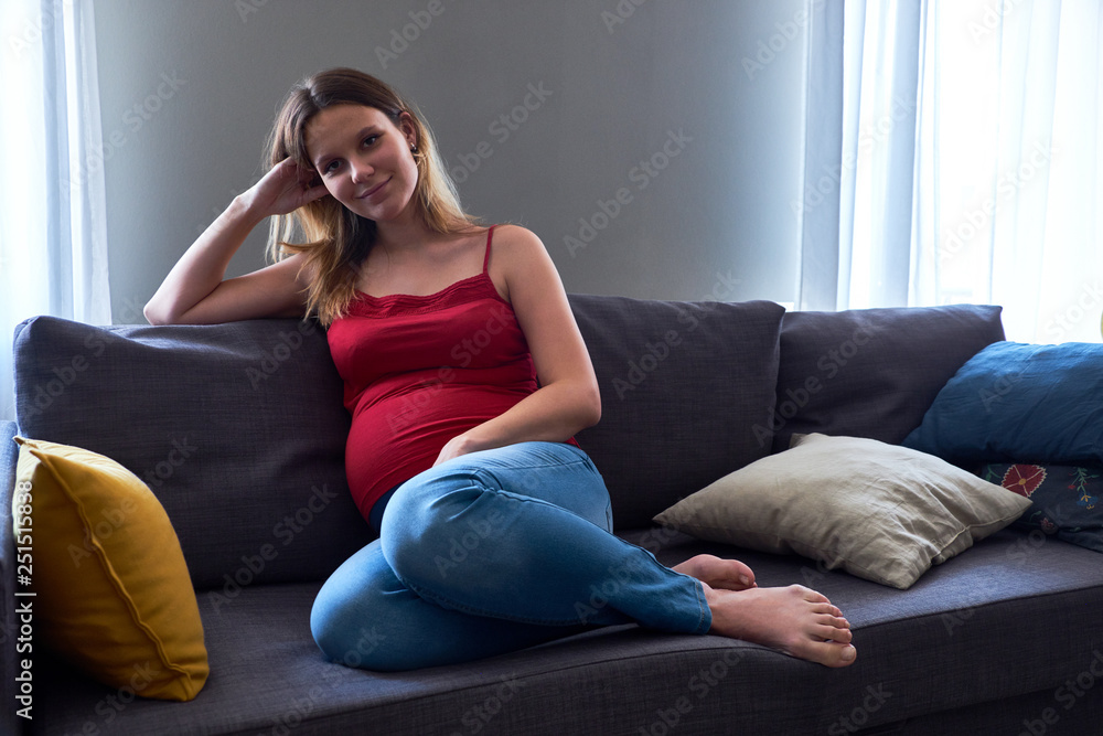 Charming pregnant young woman sitting on the sofa in the living room Charming pregnant young woman sitting on the sofa in the living room