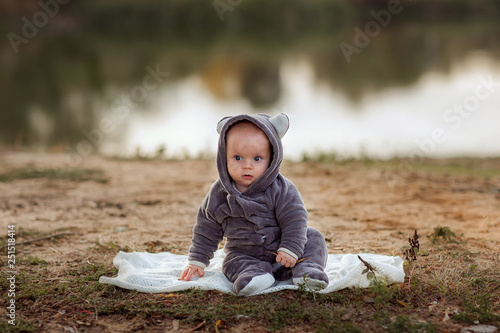 Fototapeta Naklejka Na Ścianę i Meble -  The kid in a gray suit with ears sits on the lake