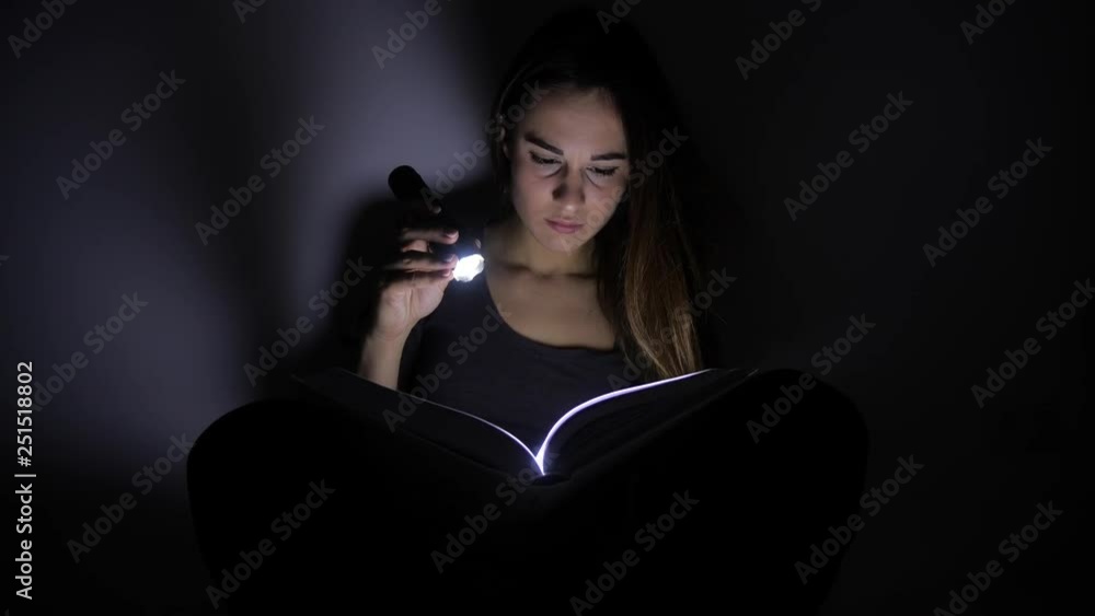 close-up portrait girl is reading a book with a flashlight in a dark room at night. 4k. Motion shooting close-up portrait girl is reading a book with a flashlight in a dark room at night. 4k. Motion shooting
