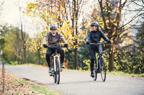 A senior couple with electrobikes cycling outdoors on a road in park in autumn. © Halfpoint